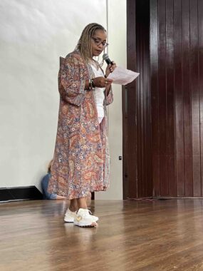 Longtime Democratic Activist Ella Jordan greets a crowd at a Women for Harris event. She wears a long colorful jacket and sneakers.