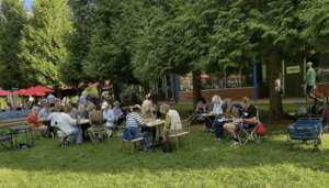 Volunteers at Ix Park near Brazos Tacos work at several tables writing postcards in tree shade.