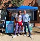 Photo of two Democrats, a black woman and a white man, in front of their tent outside a polling place