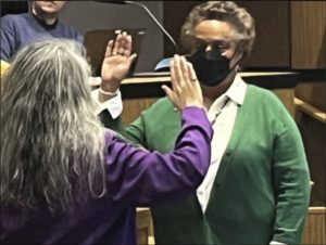 Leah Puryear faces the camera wearing a green jacket and a black COVID mask raising her hand to be sworn in by Charlottesville Clerk of Court Llezelle Dugger. Dugger is wearing a purple jacket and has her back to the camera and also has her hand raised.
