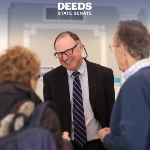 Photo of Creigh Deeds in a suit and tie talking with constituents. Caption is "Deeds State Senate"