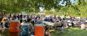 Crowd (partial) seated at long outdoor tables on the grass at Jefferson School for the Summer 2022 summer fundraiser (a fish fry that year)