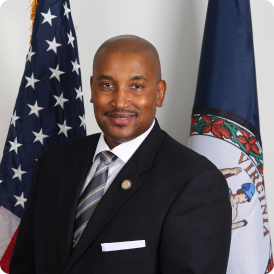 2023 Clinton Jenkins headshot wearing suit and tie with American and Virginia flags in background