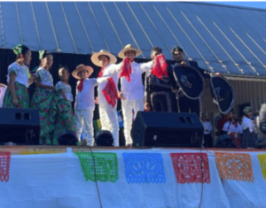 Mexican dancers in traditional costumes - women in green floral skirts men in white waving bandannas or hats to the audience.