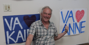 Photo of Senator Tim Kaine pointing to a poster that says "Virginia Hearts ♥️ Anne", his wife. Another poster behind him says "Virginia ♥️ Kaine."