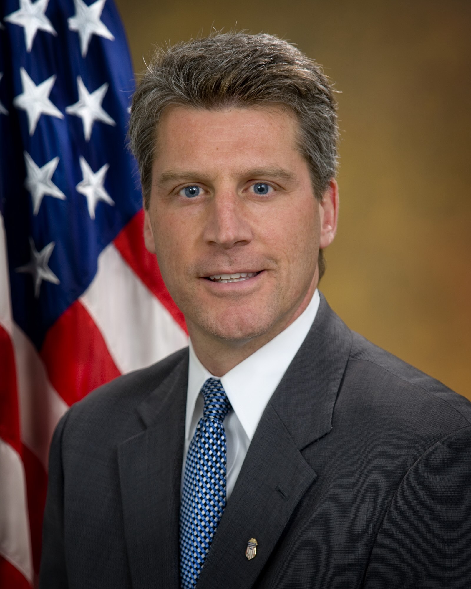 Official portrait of former US attorney Tim Heaphy in suit and tie standing in front of a US flag.