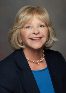 Formal portrait of Susan Swecker, retired Democratic Party of Virginia chair, wearing a pearl necklace, blue top, and dark suit jacket.